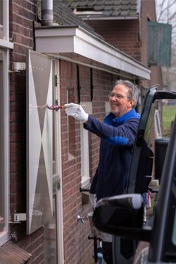 Hans van Oostrum staat een luik te schilderen in de kleuren beige wit