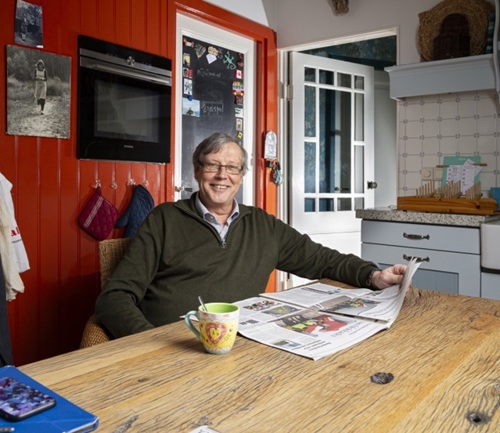 Frans Boetzkes zit aan zijn keukentafel. Hij leest de krant en lacht.