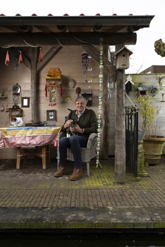 Frans Boetzkes zit in een tuinhuisje met de kat op schoot.